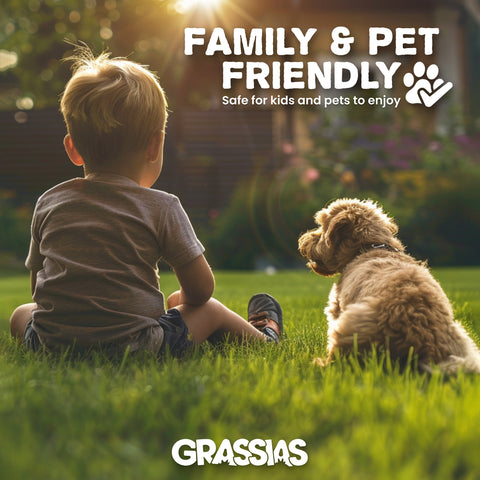 Grassias 'Family & Pet Friendly' promotional image showing the back view of a young child and a small curly-haired dog sitting together on a green lawn in golden evening sunlight, with a garden and flowers in the background. Text reads 'Safe for kids and pets to enjoy' with a paw-print hand icon.