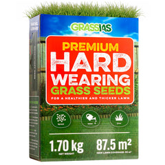 Grassias Premium Hard Wearing Grass Seeds box (1.70 kg) with a bold red and green design featuring a garden lawn background with a wooden fence and flower borders. The packaging promotes a healthier and thicker lawn, with three simple steps — Spread, Water, Grow — shown as green icons. Coverage is listed as 87.5 m², with new lawn coverage of 50 m². The box includes a built-in seed applicator and tips for success on the side panel.