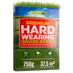 Grassias Premium Hard Wearing Grass Seeds box (750 g) with a bold red and green design featuring a garden background with a wooden fence and colourful flower borders. The packaging promotes a healthier and thicker lawn, with three simple steps — Spread, Water, Grow — shown as green icons. Coverage is listed as 37.5 m², with new lawn coverage of 21 m².
